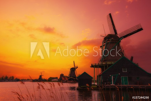 Bild på Traditional Dutch windmills on the canal bank at warm sunset light in Netherlands near Amsterdam